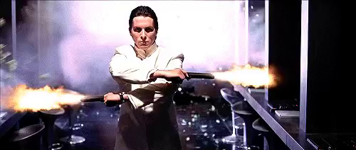 The actor Christian Bale, in the movie Equilibrium walking down an office coridor, wielding dual pistols, wearing a slightly bloodied suit, shooting at monitors and screens that were used to show and fabricate propaganda.